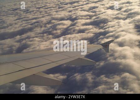 Flugzeugflügel, der während eines goldenen Sonnenaufgangs über einer dichten Wolkenschicht schwingt Stockfoto