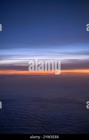 Sonnenuntergang aus einer Ebene über den Wolken, mit einem Gradient von Orange und Blau über dem Himmel Stockfoto