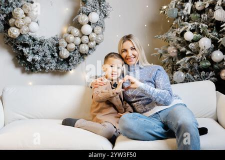 Mutter und ihre beiden Söhne sitzen auf einer weißen Couch in einem weihnachtlich dekorierten Wohnzimmer Stockfoto