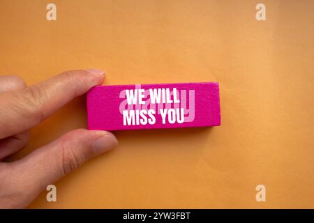 Wir werden Ihre Nachricht vermissen, geschrieben auf rosafarbenem Holzblock mit orangem Hintergrund. Konzeptionell werden wir dich vermissen Symbol. Kopierbereich. Stockfoto