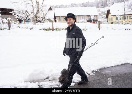 Ein Schornsteinfeger geht durch ein schneebedecktes Viertel, mit Werkzeugen. Das Bild zeigt einen Winterarbeitstag mit traditionellem Schornsteinfeger Stockfoto