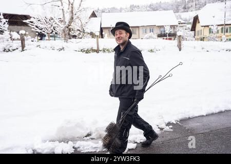 Ein Schornsteinfeger geht durch ein schneebedecktes Viertel, mit Werkzeugen. Das Bild zeigt einen Winterarbeitstag mit traditionellem Schornsteinfeger Stockfoto