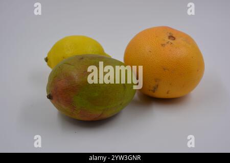 Gesundheit, gesunde Lebensmittel, Früchte, geeignete Ernährung. Eine grün-rote Mango, eine gelbe Zitrone, eine rot-orange Grapefruit auf weißem mattem Hintergrund. Stockfoto