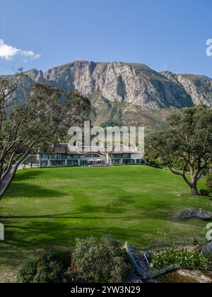 Großes Haus am Fuße des hohen felsigen Berges, Gebäude, hellgrün idealer Rasen, Hotelgebiet. Hermanus Klein Lagune, Kleinriversvlei, Fluss Stockfoto