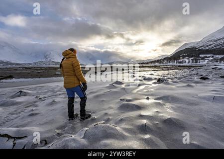 Eine Frau in Winterkleidung am gefrorenen Ufer des Ullsfjords, Sjursnes, Tromso, Troms, Norwegen, Europa Stockfoto