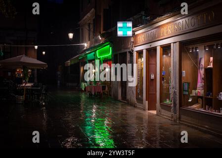 Stadtlichter von Venedig: Schaufenster und eine leere Straße im historischen Cannaregio-Viertel bei regnerischer Nacht. Stockfoto