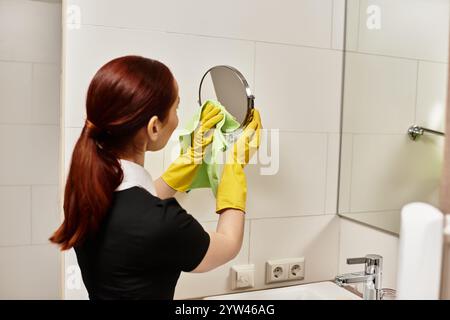 Eine junge Frau wischt vorsichtig einen Spiegel ab und sorgt so für eine klare Reflexion in einem stilvollen Badezimmer. Stockfoto