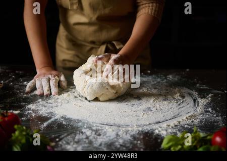 Eine Person kntet Teig auf einem bemehlten Tisch und zeigt den Prozess des Backens zu Hause. Stockfoto