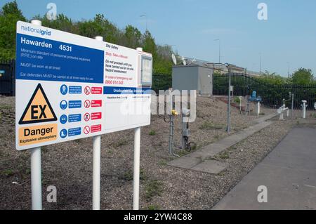 Ein Sicherheitshinweisschild für den Standort mit Gefahrensymbolen an der Einrichtung des nationalen Netzes für geruchsneutrale Gase, mit einem Teil der Anlage in Sichtweite, Nordwales Stockfoto