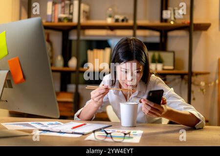 Eine junge Frau, die bis spät in die Nacht arbeitet und Instant-Nudeln zum Abendessen isst Stockfoto