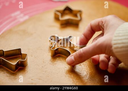 Frau, die Keksschneider benutzt, um Lebkuchenteig auf roter Matte zu Formen. Traditionelle Weihnachtskekse in der Küche backen Stockfoto