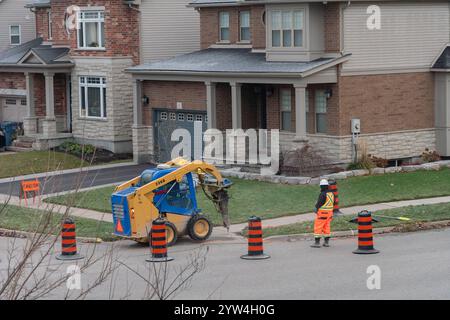 Ein kleiner Traktor mit Meißel bricht eine Betonplatte auf dem Gehweg, um ein neues Kabel unter die Straße zu legen Stockfoto