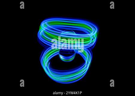 Abstrakte blaue und grüne Lichtspuren, die durch Lichtmalerei um eine statische Glaskugel auf einem Spiegel vor einem schlichten schwarzen Hintergrund entstanden sind Stockfoto