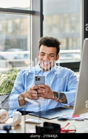 Ein fröhlicher Mann lächelt weit, wenn er sein Smartphone an einem modernen Arbeitsplatz bedient. Stockfoto