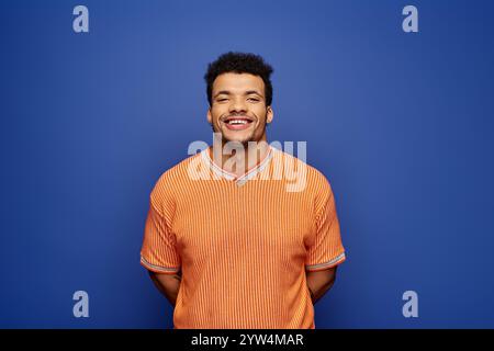 Ein fröhlicher Mann in einem orangefarbenen Hemd lächelt vor einem auffälligen blauen Hintergrund. Stockfoto