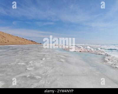 Die gefrorene Landschaft zeigt Eisschichten entlang eines Strandes mit Eisbrocken, die den Kontrast zum blauen Himmel betonen. Stockfoto