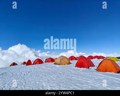 Zelte in verschiedenen Farben besetzen eine schneebedeckte Landschaft, umgeben von Wolken und sonnen sich im hellen Nachmittagssonnenlicht. Stockfoto