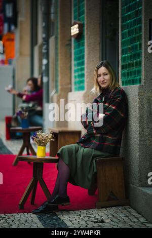 Eine Frau sitzt in einem Open-Air-Café und strahlt eine warme Vorweihnachtsstimmung aus. Stockfoto
