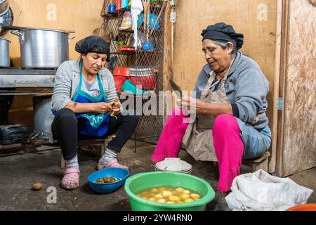 Lurin, Peru — 29. Juli 2023: Zwei Frauen waschen, schneiden und schälen Kartoffeln gemeinsam in Eimern in der bescheidenen Gemeinschaftsküche Stockfoto