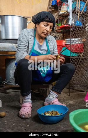 Lurin, Lima, Peru – 6. September 2024: Peruanische Frau mit schwarzem Küchenhut schneidet und schält Kartoffeln zusammen in einem Eimer in der Gemeinschaftsküche Stockfoto