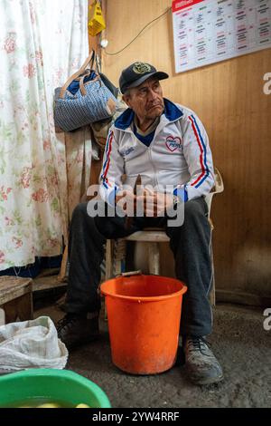 Lurin, Peru – 6. September 2024: Der alte Mann schält Kartoffeln über einem Orangeneimer in der Gemeinschaftsküche Stockfoto