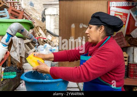Lurin, Lima, Peru – 6. September 2024: Eine peruanische Frau in Rot gekleidet mit einem schwarzen Küchenhut wäscht Kürbisstücke in einem Eimer im kommunalen Ki Stockfoto