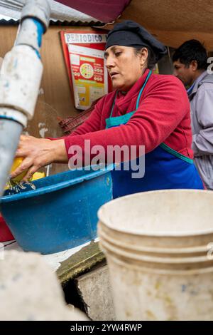 Lurin, Lima, Peru – 6. September 2024: Eine peruanische Frau in Rot gekleidet mit einem schwarzen Küchenhut wäscht Kürbisstücke in einem Eimer im kommunalen Ki Stockfoto