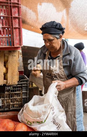 Lurin, Lima, Peru – 6. September 2024: Eine ältere Frau mit schwarzem Küchenhut greift Kartoffeln und legt sie in einen weißen Sack für die Lagerung in der Comm Stockfoto