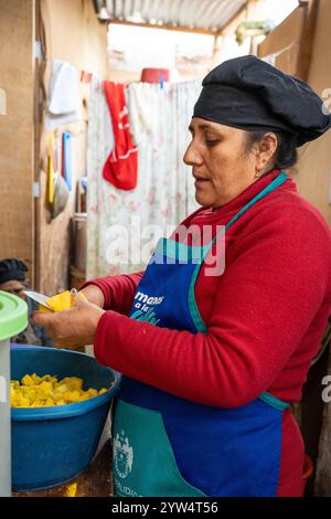 Lurin, Lima, Peru – 6. September 2024: Frau in Rot gekleidet mit schwarzem Küchenhut schneidet und schält Kartoffeln zusammen in Eimern in der Gemeinschaftsküche Stockfoto