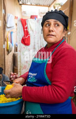 Lurin, Lima, Peru – 6. September 2024: Frau in Rot gekleidet mit schwarzem Küchenhut schneidet und schält Kartoffeln zusammen in Eimern in der Gemeinschaftsküche Stockfoto