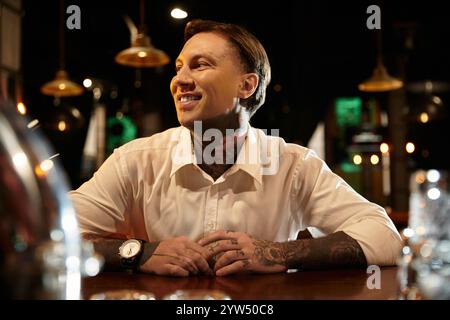 Ein tätowierter junger Mann sitzt bequem an der Bar, lächelt und genießt den Abend. Stockfoto