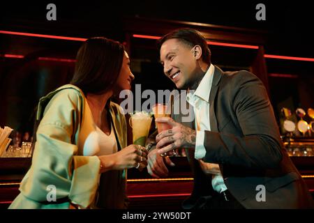 Ein tätowierter Mann und eine Frau teilen sich Lachen und Cocktails während eines lebhaften Abends. Stockfoto