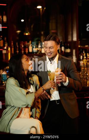 Ein junges Paar teilt fröhliche Momente, während es in einer lebhaften Bar ihre Drinks trinkt. Stockfoto