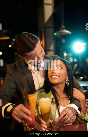 Tätowierte junge Paare teilen fröhliche Momente an einer Bar und schlürfen bei einem Date an lebhaften Cocktails. Stockfoto