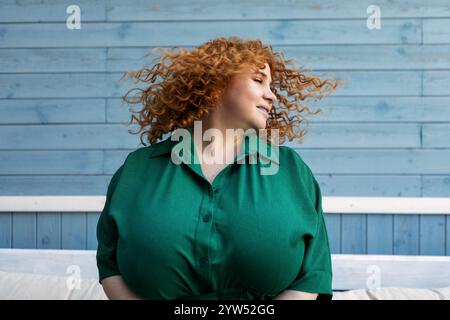 Schöne Happy Plus Size Frau genießt das Leben, tanzt und schüttelt Haare mit Freude, Selbstvertrauen und positiven Emotionen draußen vor blauem Hintergrund Stockfoto