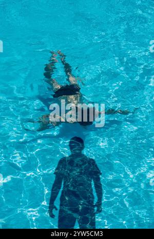 Frau im Schwimmbad mit finsterem Schatten des Mannes Stockfoto