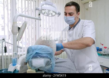 Männlicher Zahnarzt, der mit älteren Patienten in der zahnärztlichen Klinik arbeitet. Stomatologe in Schutzmaske arbeitet mit dem Zahn des Seniorenpatienten Stockfoto