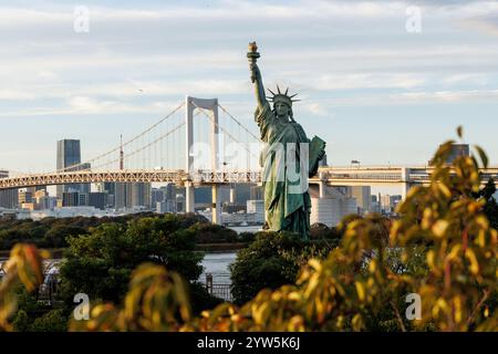 Die Freiheitsstatue steht hoch, eingerahmt von Grün und einer modernen Brücke innerhalb des pulsierenden Stadtbildes Stockfoto