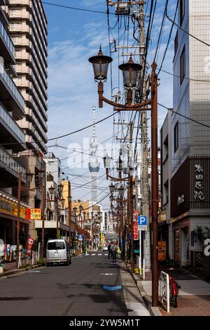 Eine belebte Straße in Tokio mit zahlreichen Stromleitungen und hohen Gebäuden, in der der berühmte Skytree von Tokio zu sehen ist Stockfoto