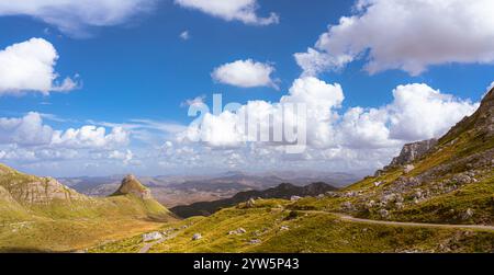 Weitläufige Berglandschaft mit grünen Tälern und einem leuchtend blauen Himmel voller Wolken. Stockfoto