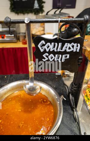 Warme Gulasch-Suppe wird auf einem geschäftigen Weihnachtsmarkt in Budapest serviert. Die Atmosphäre ist lebhaft, da die Besucher lokale Köstlichkeiten und Urlaub genießen Stockfoto