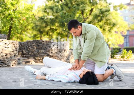 Junger Mann, der bewusstlose Frauen mit Herzinfarkt auf der Straße belebt Stockfoto