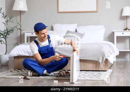 Männlicher Techniker mit Schraubendreher, der elektrische Konvektorheizung im Schlafzimmer repariert Stockfoto