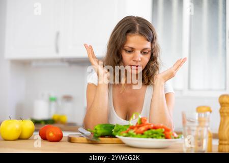 Traurige Frau, die in der Küche Gemüsesalat isst Stockfoto