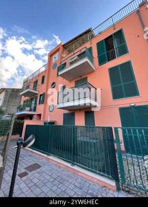 Pulsierendes pinkfarbenes Apartmentgebäude mit grünen Fensterläden und Balkonen vor einem hellblauen Himmel. Urbanes Wohnen und Wohnen. Ideal für Stockfoto