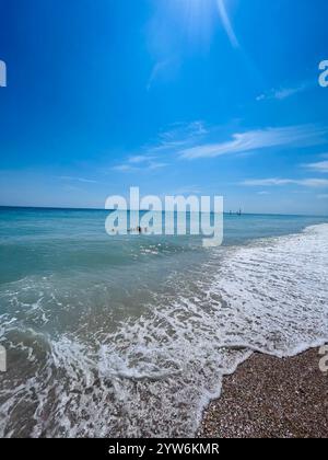 Eine ruhige Strandszene mit sanften Wellen, die unter einem leuchtend blauen Himmel gegen die Küste schlagen und Ruhe und Entspannung wecken. Ideal für Projekte mit foc Stockfoto