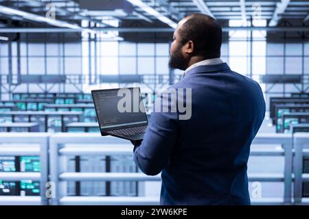 IT-Mitarbeiter im Rechenzentrum implementieren Backup-Lösungen zum Schutz vor Verlust von Infrastrukturdaten mithilfe eines Laptops. IT-Profi, der technische Probleme bei Rigs mit Notebook löst Stockfoto