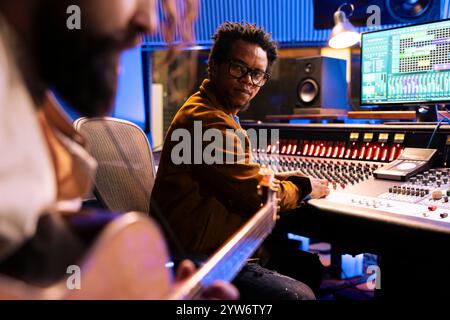 Junger Musiker, der elektroakustische Gitarre spielt und Melodien im Studio aufnimmt, mit Musikinstrumenten neue Tracks komponiert. Sänger und Sounddesigner arbeiten an einem neuen Pop-Rock-Album. Stockfoto