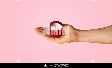 Unerkennbarer Mann, der Box mit Verlobungsring auf orangefarbenem Hintergrund hält, Nahaufnahme Stockfoto