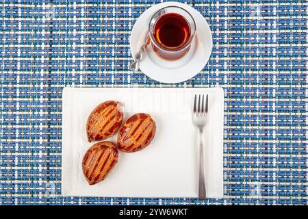 Traditionelles türkisches Dessert mit Tee: Sekerpare. Sekerpare wird mit Tee auf einem weißen Teller serviert. Stockfoto